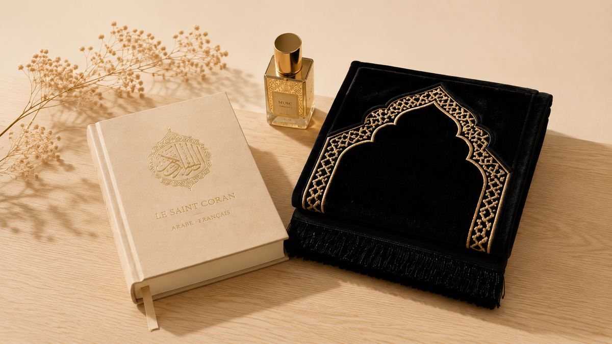 Coran bilingue arabe-français, flacon de musc et tapis de prière en velours noir à motifs mihrab dorés, posés sur une table en bois clair